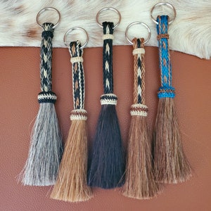 Può includere: Cinque portachiavi in ​​cuoio intrecciato con nappe di crine di cavallo in vari colori, tra cui nero, marrone, bianco e blu.