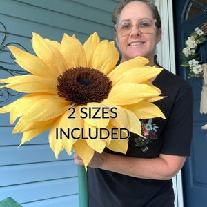Puede incluir: Un girasol amarillo grande hecho a mano con un centro marrón oscuro texturizado. La flor presenta pétalos arrugados en capas y está unida a un tallo verde. El texto "2 SIZES INCLUDED" está impreso en negro sobre el centro del girasol.