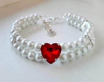 May include: A white pearl bracelet with a red heart-shaped rhinestone in the center.