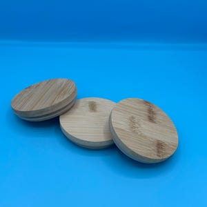May include: Three round wooden lids with a natural wood grain finish. The lids are made of bamboo and have a white rubber seal around the edge.