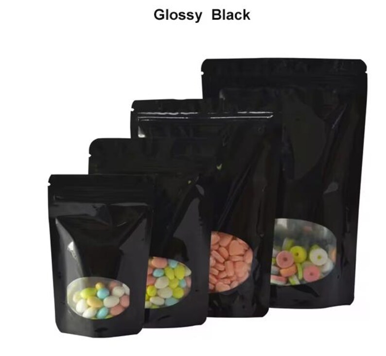 May include: Four black stand-up pouches with clear oval windows, the smallest pouch is filled with colorful candies, the next size up is filled with pastel candies, the next size up is filled with pink heart-shaped candies, and the largest pouch is empty.  Glossy Black.