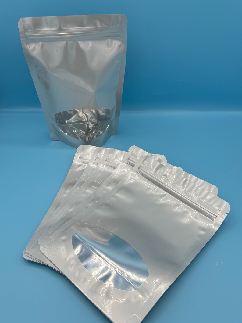 May include: A stack of white stand-up pouches with a clear oval window. The pouches have a zipper closure.