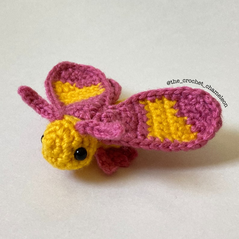May include: A crocheted butterfly with yellow and pink wings. The butterfly has black eyes and is made with a soft yarn.