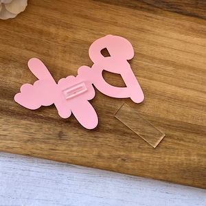 Puede incluir: Un letrero de acrílico rosa "Baby" con una tira adhesiva transparente en la parte posterior.