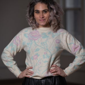 Könnte beinhalten: Eine Frau mit grauem Haar trägt einen weißen Pullover mit einem floralen Muster in Rosa und Blau. Sie trägt auch eine schwarze Lederhose.