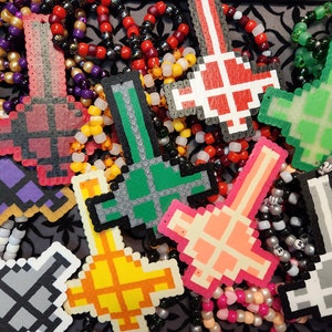 May include: A collection of colorful pixelated keychains featuring various designs, including swords, hearts, and geometric shapes. The keychains are made of plastic beads and are strung together on a cord.
