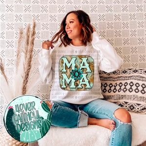 Puede incluir: Una sudadera blanca con la palabra "MAMA" impresa en ella en una fuente desgastada de color turquesa y marr&oacute;n. Las letras est&aacute;n decoradas con joyas turquesas y marrones. La sudadera la lleva puesta una persona.