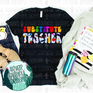 May include: A black t-shirt with the text "Substitute Teacher" in colorful letters. The letters are decorated with school-themed images like apples, pencils, and books. The shirt is laid out on a table with a white blanket, a coffee mug, and a notebook.