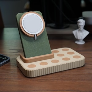 May include: A multi-device charging station in olive green, beige, and brown. The station features a wireless charging pad for a phone and a base with multiple circular charging spots. A white and beige wireless charger is attached to the green stand.