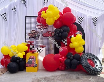 May include: A Cars themed birthday party decoration with red, yellow, and black balloons, a black grid backdrop, and a sign that says "Fabian 2".