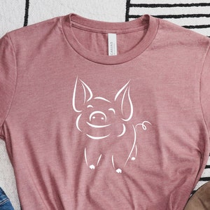 May include: A mauve t-shirt with a white outline of a smiling pig.