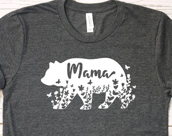 May include: A dark gray t-shirt with a white silhouette of a bear with the word "Mama" inside the bear. The bear is filled with floral designs and butterflies.