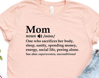 May include: A light pink t-shirt with a black graphic that reads "Mom" and defines the word as "One who sacrifices her body, sleep, sanity, spending money, energy, social life, peeing alone. See also: superwomen, unconditional."