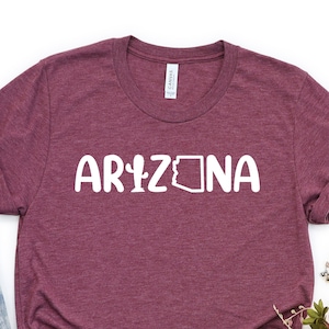 May include: A maroon t-shirt with the text "ARIZONA" in white, featuring a cactus and the outline of the state of Arizona.