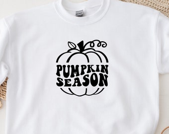 May include: White sweatshirt with a black pumpkin graphic and the words "PUMPKIN SEASON". The design features a stylized pumpkin with a stem and curly vines. The sweatshirt is made of a soft material, perfect for fall.