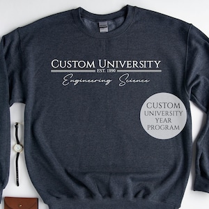 May include: A dark blue sweatshirt with the text "CUSTOM UNIVERSITY EST. 1890 Engineering Science" printed on the front. The text is in white and has a vintage look. The sweatshirt is made of a soft, comfortable material.