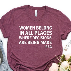 May include: A maroon t-shirt with the text "Women belong in all places where decisions are being made - RBG" printed in white.