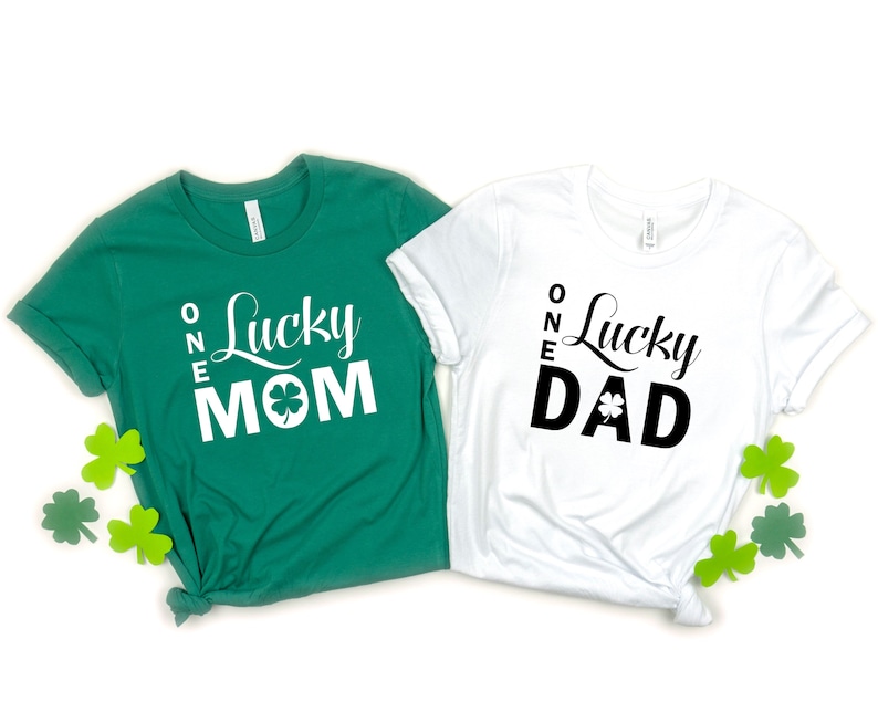 May include: Two green and white t-shirts with the text "One Lucky Mom" and "One Lucky Dad" printed on them. Each shirt has a shamrock graphic.