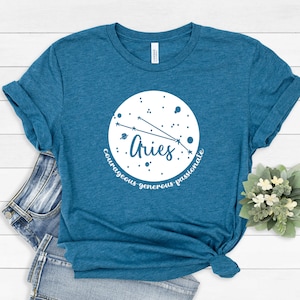 Pu&ograve; includere: T-shirt blu turchese con una grafica circolare bianca che presenta il segno zodiacale Ariete e le parole "coraggioso, generoso, passionale".