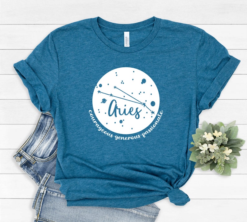 Pu&ograve; includere: T-shirt blu turchese con una grafica circolare bianca che presenta il segno zodiacale Ariete e le parole "coraggioso, generoso, passionale".