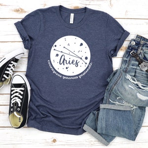 Pu&ograve; includere: Una t-shirt blu navy con un grafico circolare bianco che presenta la costellazione dell'Ariete e le parole "Ariete, coraggioso, generoso, passionale".