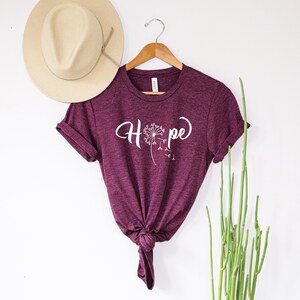 May include: Burgundy t-shirt with a white dandelion graphic and the word "Hope" in a cursive font.