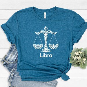 Op de afbeelding: Een tealblauw t-shirt met een wit Libra-sterrenbeeld en het woord "Libra" gedrukt op de voorkant.