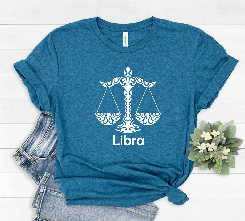 Op de afbeelding: Een tealblauw t-shirt met een wit Libra-sterrenbeeld en het woord "Libra" gedrukt op de voorkant.