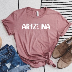 May include: A mauve t-shirt with the text "ARIZONA" in white with a cactus and the outline of the state of Arizona.