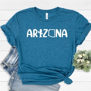 May include: A teal blue t-shirt with the text "ARIZONA" in white, featuring a cactus and the outline of the state of Arizona.