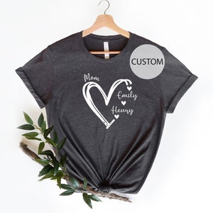 K&ouml;nnte beinhalten: Ein dunkelgraues T-Shirt mit einem wei&szlig;en Herzdesign. Das Herz tr&auml;gt oben das Wort "Mom" und die Namen "Emily" und "Henry" im Herzen.