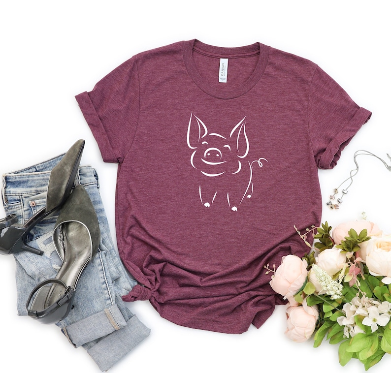 May include: A maroon t-shirt with a white outline of a smiling pig on the front.