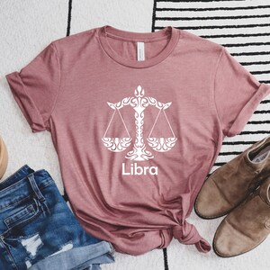 Op de afbeelding: Een mauve t-shirt met een wit Libra sterrenbeeld symbool en het woord "Libra" erop gedrukt.