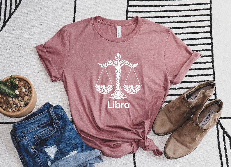 Op de afbeelding: Een mauve t-shirt met een wit Libra sterrenbeeld symbool en het woord "Libra" erop gedrukt.