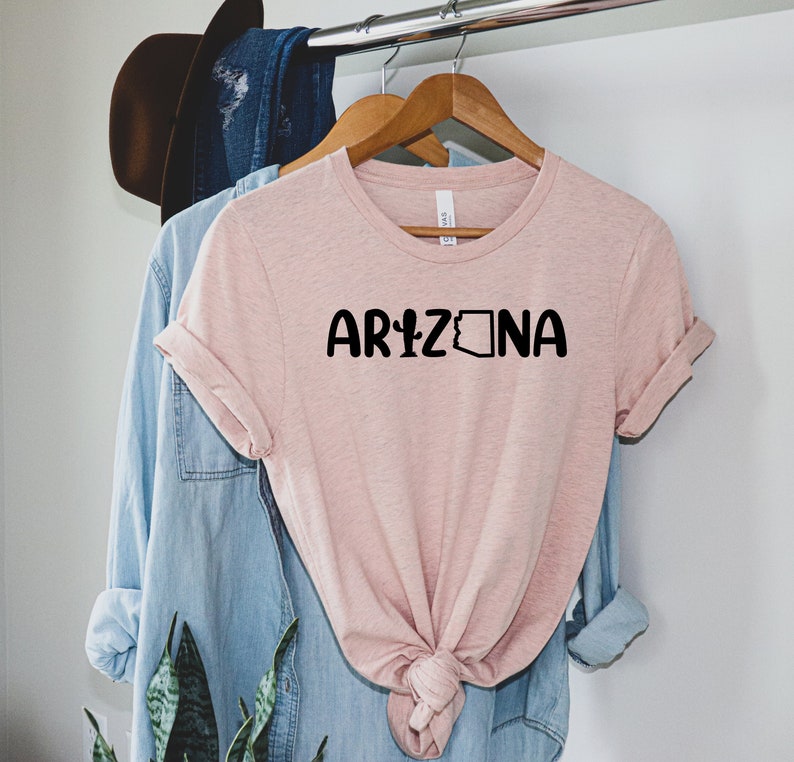 May include: A pink t-shirt with the text "ARIZONA" in black lettering. The text includes a cactus and the outline of the state of Arizona.