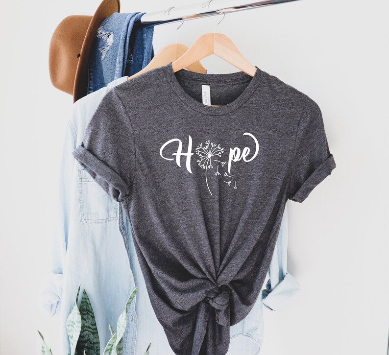 May include: A dark gray t-shirt with a white dandelion graphic and the word "Hope" written in a cursive font.