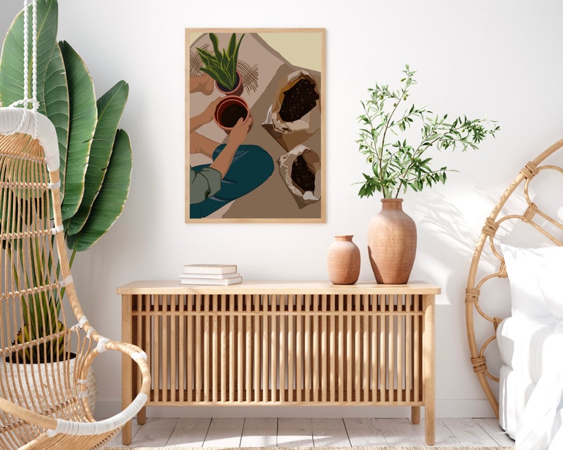 May include: A digital illustration of a person potting plants. The illustration is in a brown frame and hangs on a white wall. The person is wearing blue jeans and a light blue shirt. The person is holding a brown pot with a green plant in it. There are two brown paper bags with soil in them. The illustration is in a minimalist style.