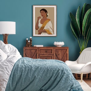 May include: A bedroom interior with a teal blue wall, a white bed with a blue blanket, a wooden dresser, a white chair, and a framed illustration of a woman wearing a white and gold sari.