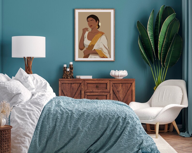 May include: A bedroom interior with a teal blue wall, a white bed with a blue blanket, a wooden dresser, a white chair, and a framed illustration of a woman wearing a white and gold sari.