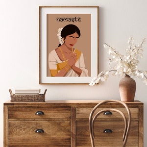 May include: A digital illustration of a woman in a white and gold sari with her hands clasped in a prayer position. The background is a light brown color and the text "namaste" is written in black at the top of the image.