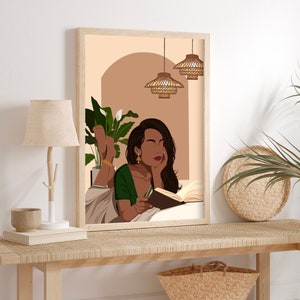 May include: A framed illustration of a woman reading a book while lying down. She is wearing a green and white sari and has long dark hair. The background is a light brown color with a plant in the corner and three hanging light fixtures.