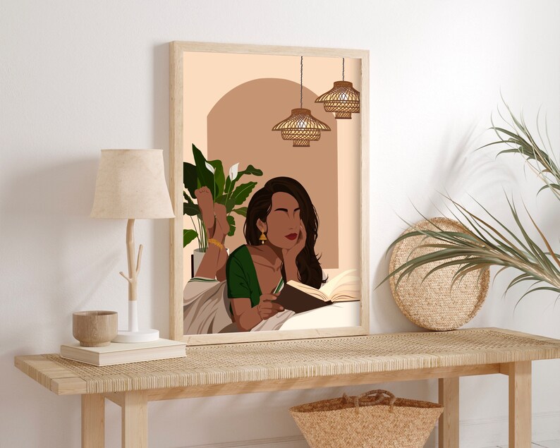 May include: A framed illustration of a woman reading a book while lying down. She is wearing a green and white sari and has long dark hair. The background is a light brown color with a plant in the corner and three hanging light fixtures.