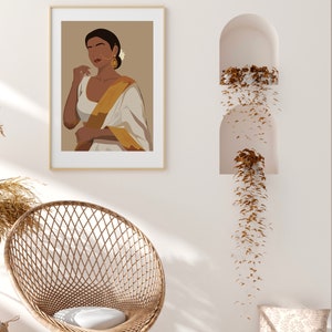 May include: A digital illustration of a woman wearing a white and gold sari with a flower in her hair. The illustration is framed and hanging on a white wall.
