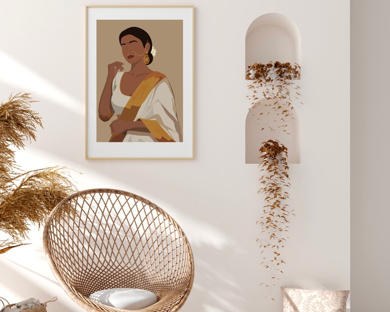 May include: A digital illustration of a woman wearing a white and gold sari with a flower in her hair. The illustration is framed and hanging on a white wall.