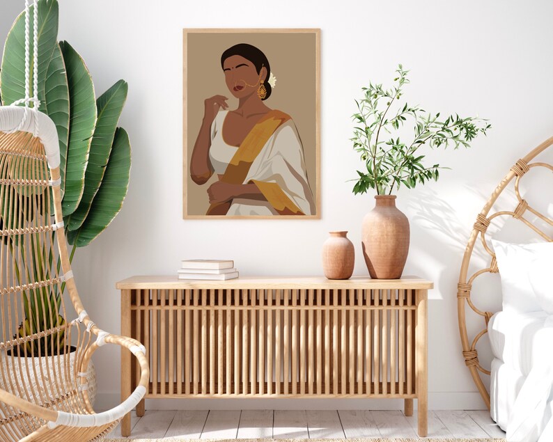 May include: A framed illustration of a woman wearing a white and gold sari with a brown background. The woman is looking to the side and has dark hair and brown eyes. She is wearing gold earrings and a nose ring.