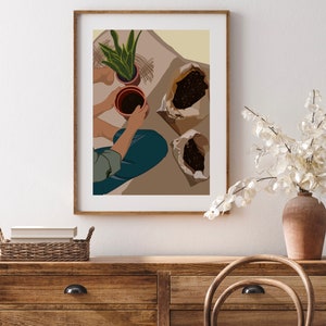 May include: A person is potting plants. They are holding a brown pot with soil in it. There are two bags of soil on the floor. The background is a light beige color.