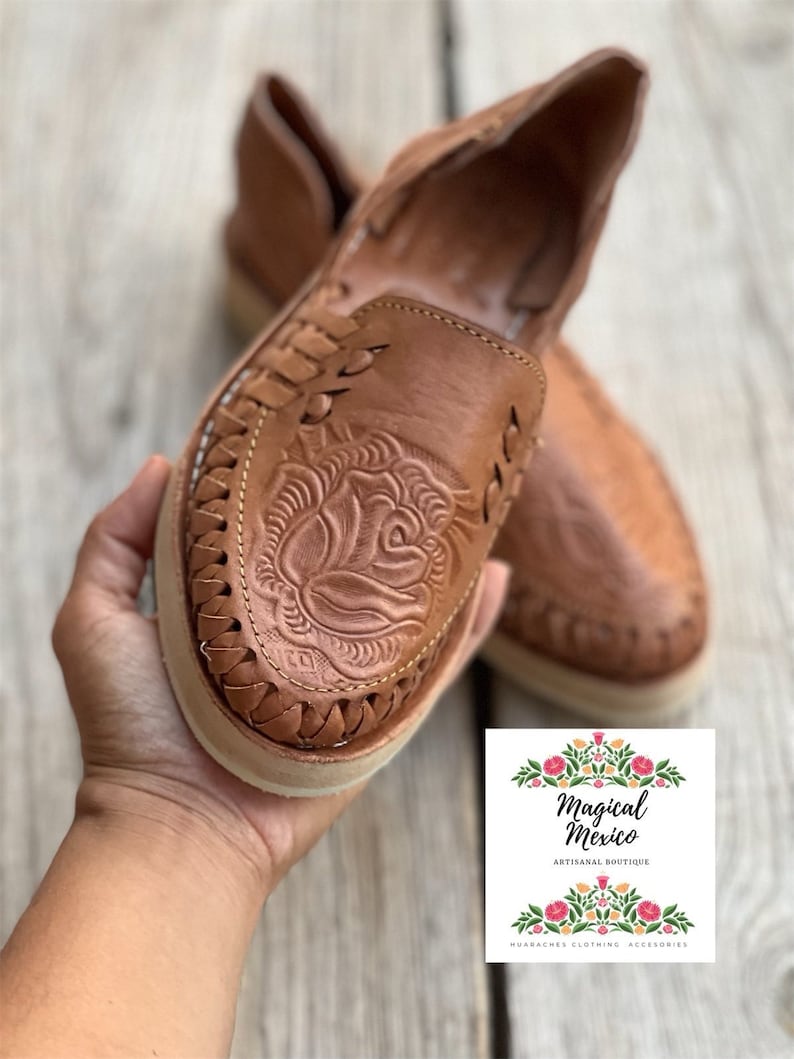 Peut inclure: Paire de huaraches en cuir marron avec un motif floral en relief sur le dessus. Les chaussures ont un motif tress&eacute; sur les bords et une semelle cr&egrave;me. Le logo "Magical Mexico" est visible.