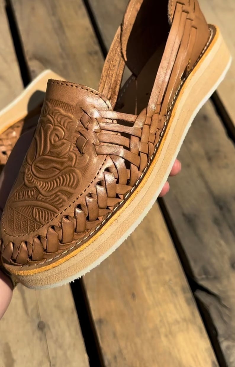 Peut inclure: Huaraches en cuir marron avec un motif tress&eacute; et une semelle plateforme. L'avant de la chaussure pr&eacute;sente des motifs floraux et g&eacute;om&eacute;triques en relief. La semelle mesure environ 2,5 cm d'&eacute;paisseur. Le mot "MEXICO" est estamp&eacute; sur la chaussure.