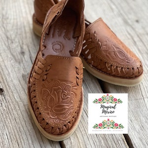 Peut inclure: Sandales huaraches en cuir marron avec un motif floral en relief. Les sandales &agrave; bout ouvert pr&eacute;sentent des d&eacute;tails tress&eacute;s et une semelle de couleur cr&egrave;me. L'image comprend le logo de Magical Mexico.