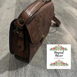 May include: Brown leather crossbody bag with embossed floral design. The bag features a flap closure with a gold-colored clasp and a long adjustable strap. The text "@magical mexico" is visible on the strap.